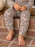 Child in leopard print pajamas sitting on brick steps with bare feet, hands clasped on knees.