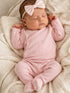 Sleeping baby girl in a pink outfit with a bow, nestled on a soft, textured blanket.