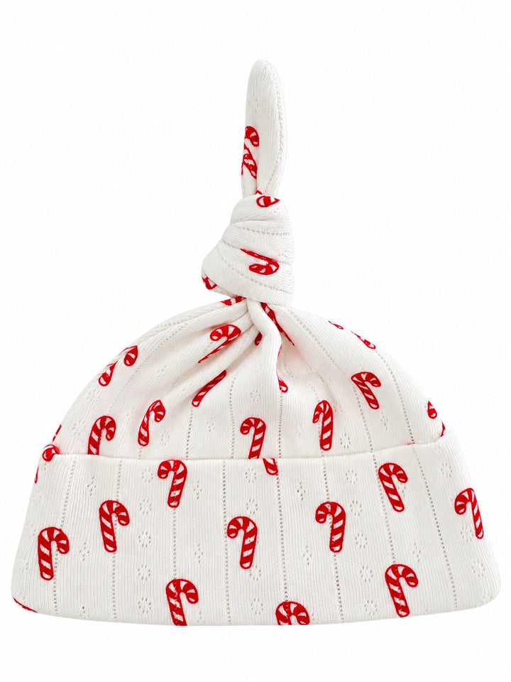 White baby hat with a knot on top, adorned with red candy cane patterns.