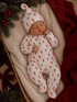 Sleeping baby in candy cane patterned pajamas, nestled in a cozy basket with blankets and holiday decorations.