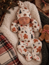 Sleeping baby in festive gingerbread-themed pajamas, nestled in a cozy blanket with holiday decorations around.