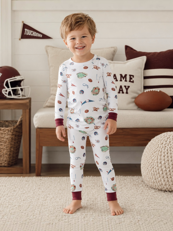 Smiling boy in patterned pajamas stands on a rug, surrounded by sports-themed decor and cozy furnishings.