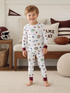 Smiling boy in patterned pajamas stands on a rug, surrounded by sports-themed decor and cozy furnishings.