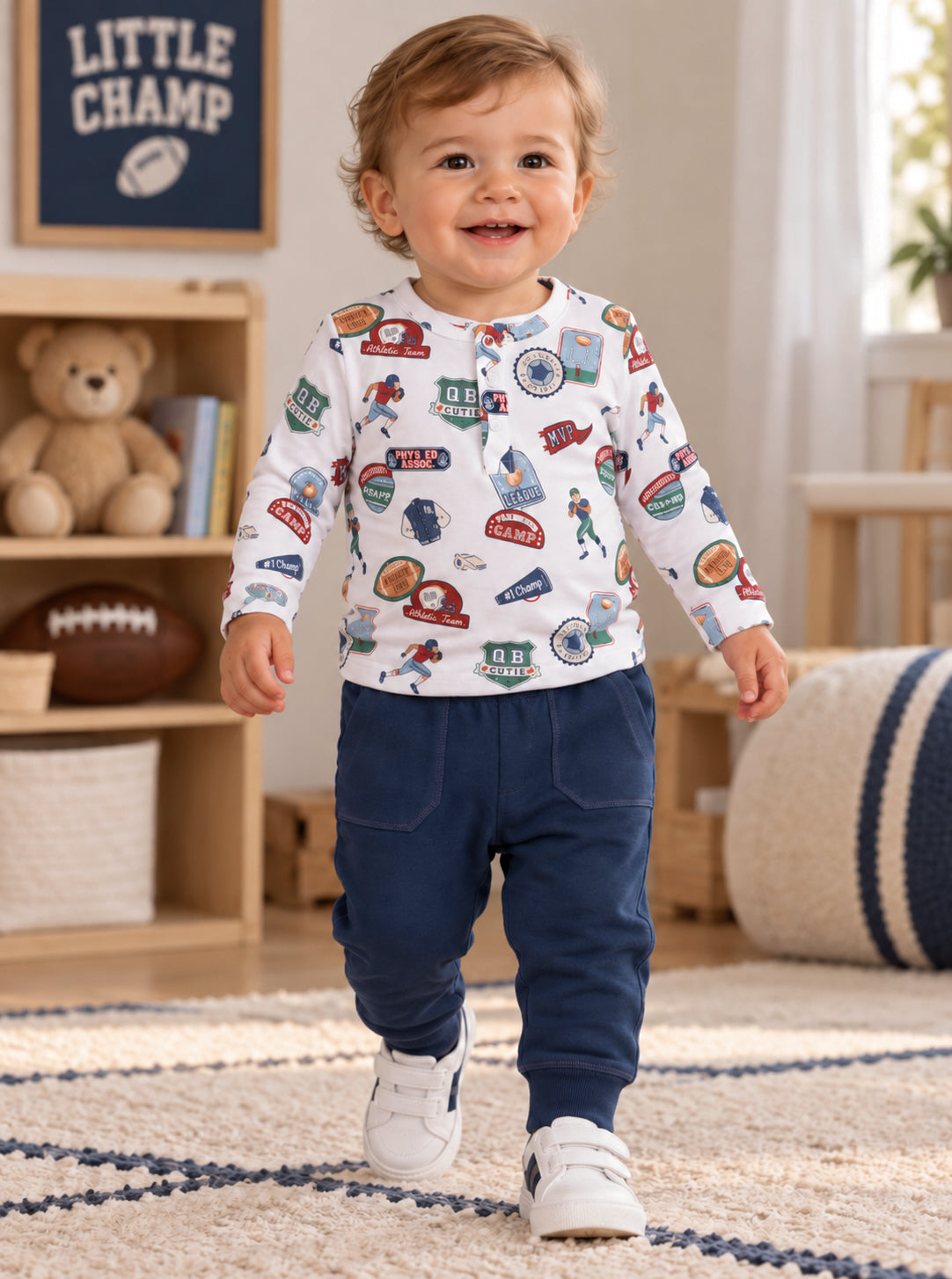 Toddler boy in playful sports-themed outfit, walking happily in a bright, cozy room.