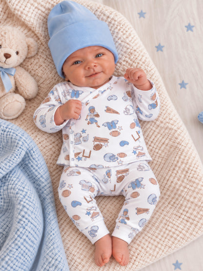 Smiling baby in a blue hat and sports-themed outfit, surrounded by plush toys and soft blankets.