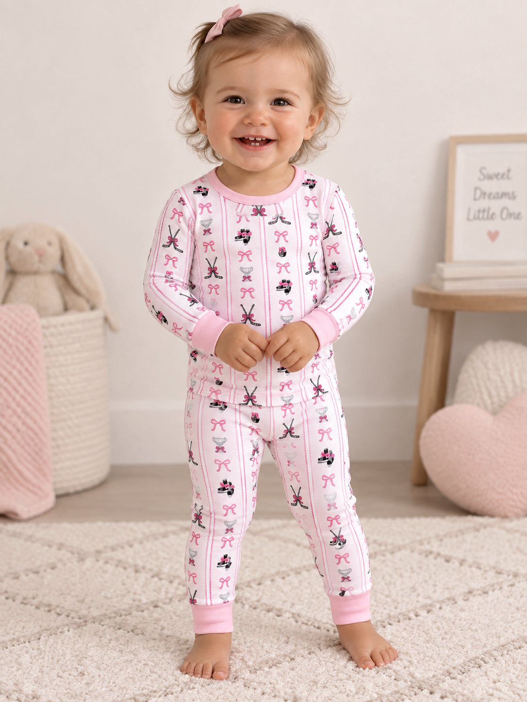 Smiling toddler in playful pink pajamas with fun patterns, standing on a soft rug.