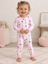 Smiling toddler in playful pink pajamas with fun patterns, standing on a soft rug.