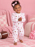 Toddler in pink patterned pajamas smiles, playing indoors with a football, surrounded by soft pink decor.
