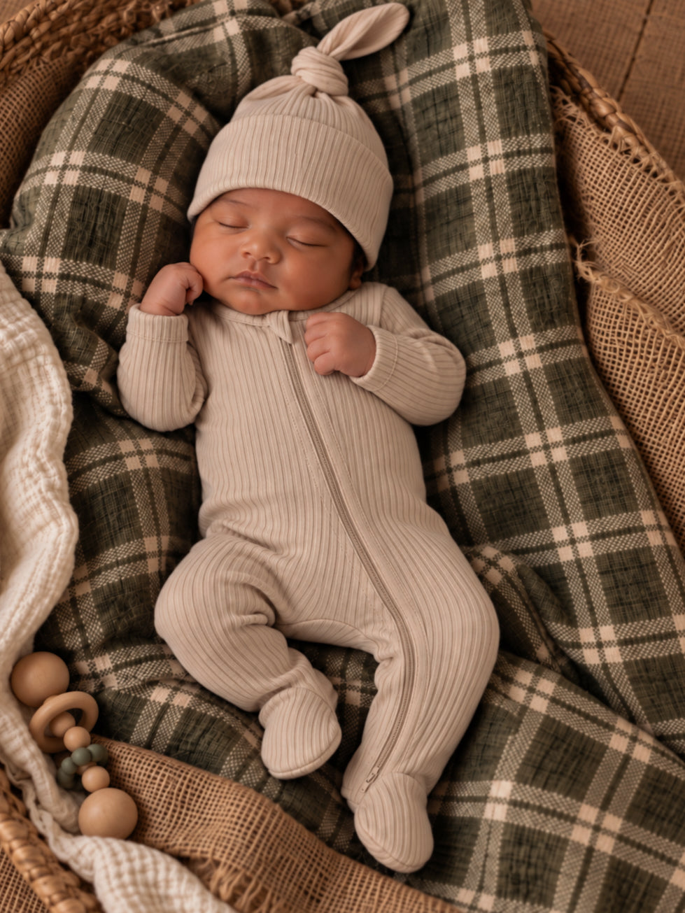 Infant sleeping in beige outfit and hat on a cozy plaid blanket, nestled in a woven basket.