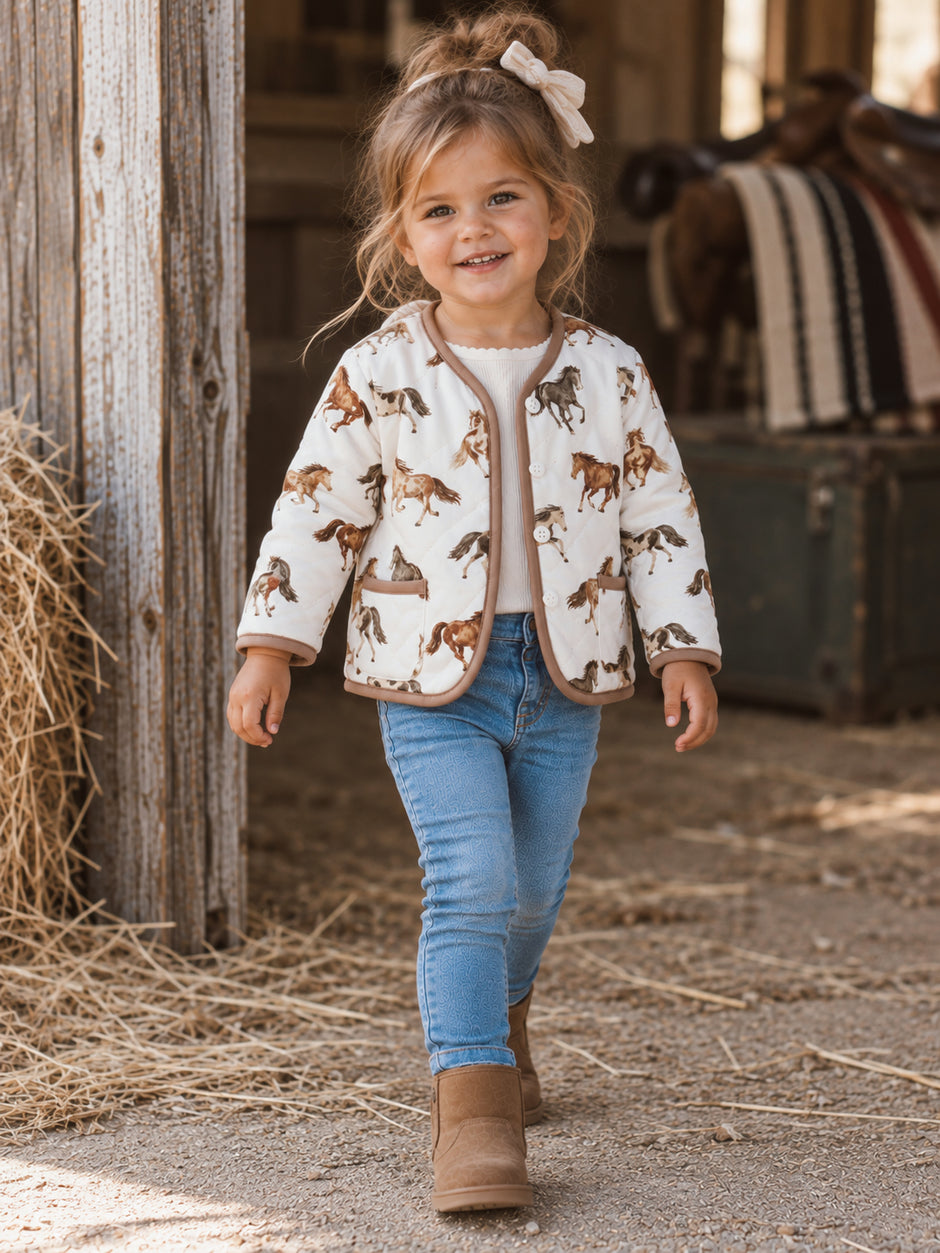 Smiling young girl in a horse-print jacket, walking on a farm path with hay around her.