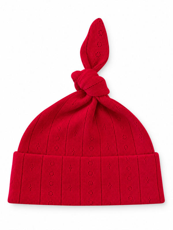 Red knit hat with a tied top, featuring a textured pattern and a turned-up brim.
