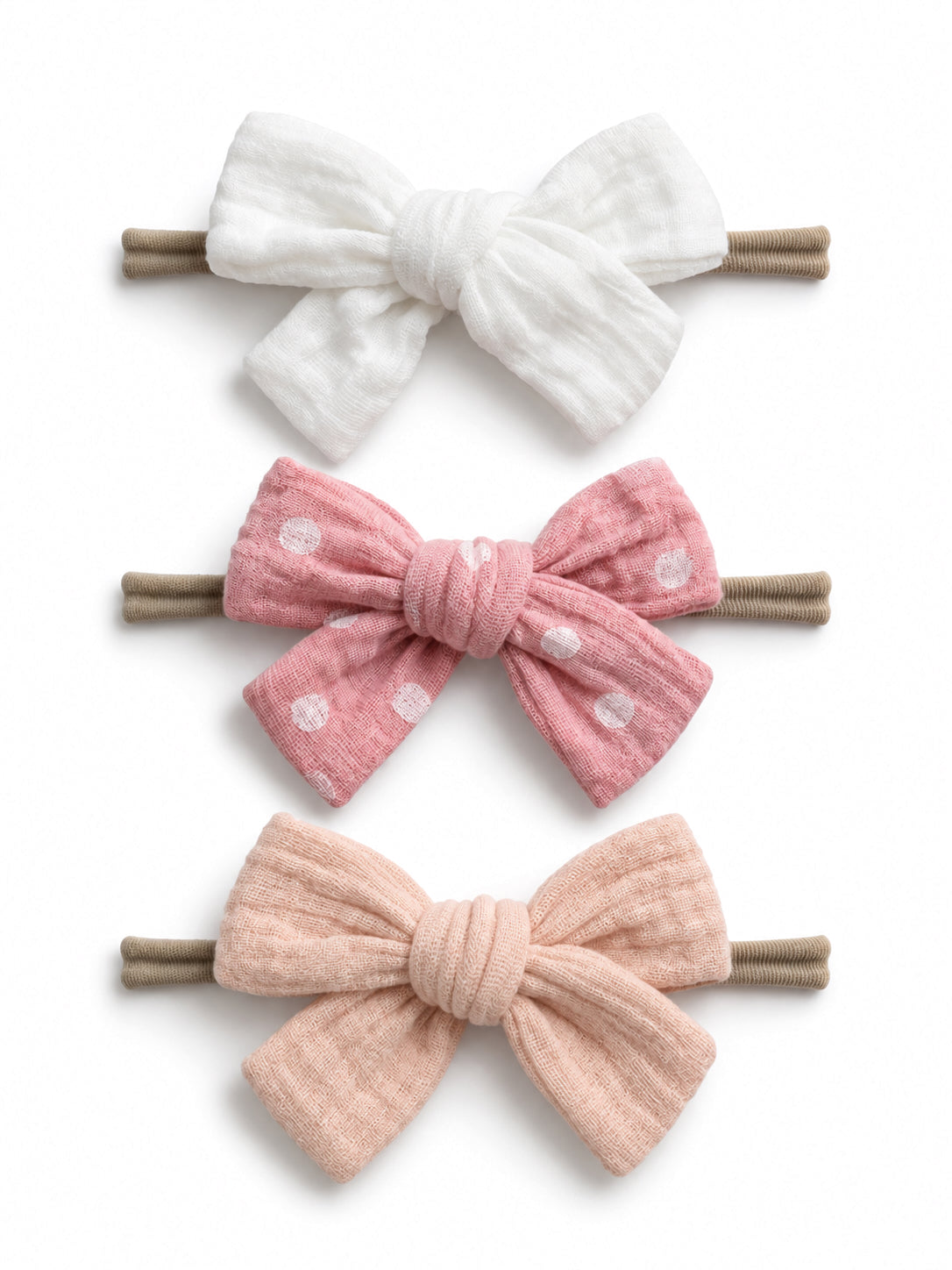 Three hair bows: white, pink with polka dots, and soft pink, all attached to brown hair elastics.