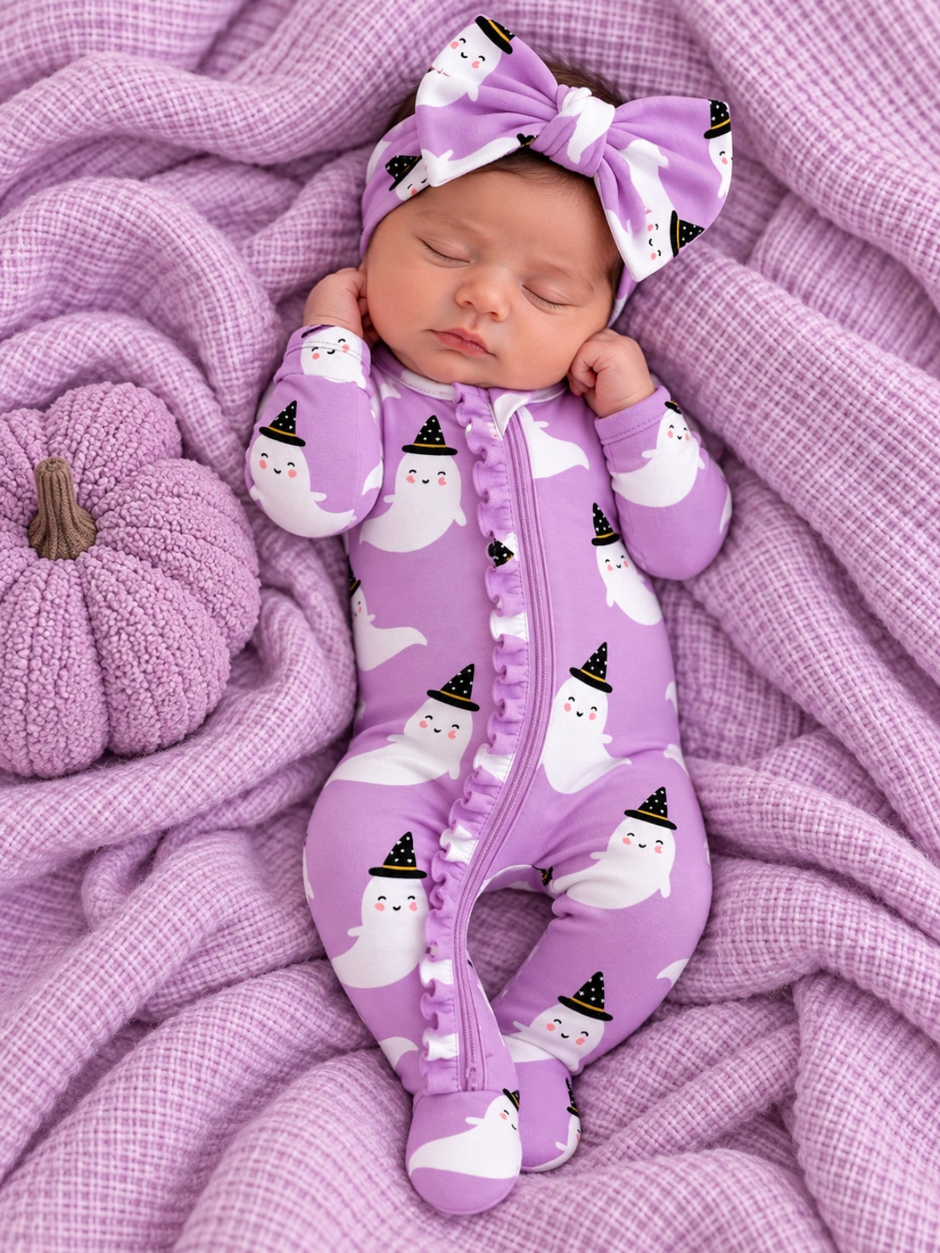 Baby girl in a purple ghost-patterned outfit and headband, resting on a soft, textured lavender blanket.