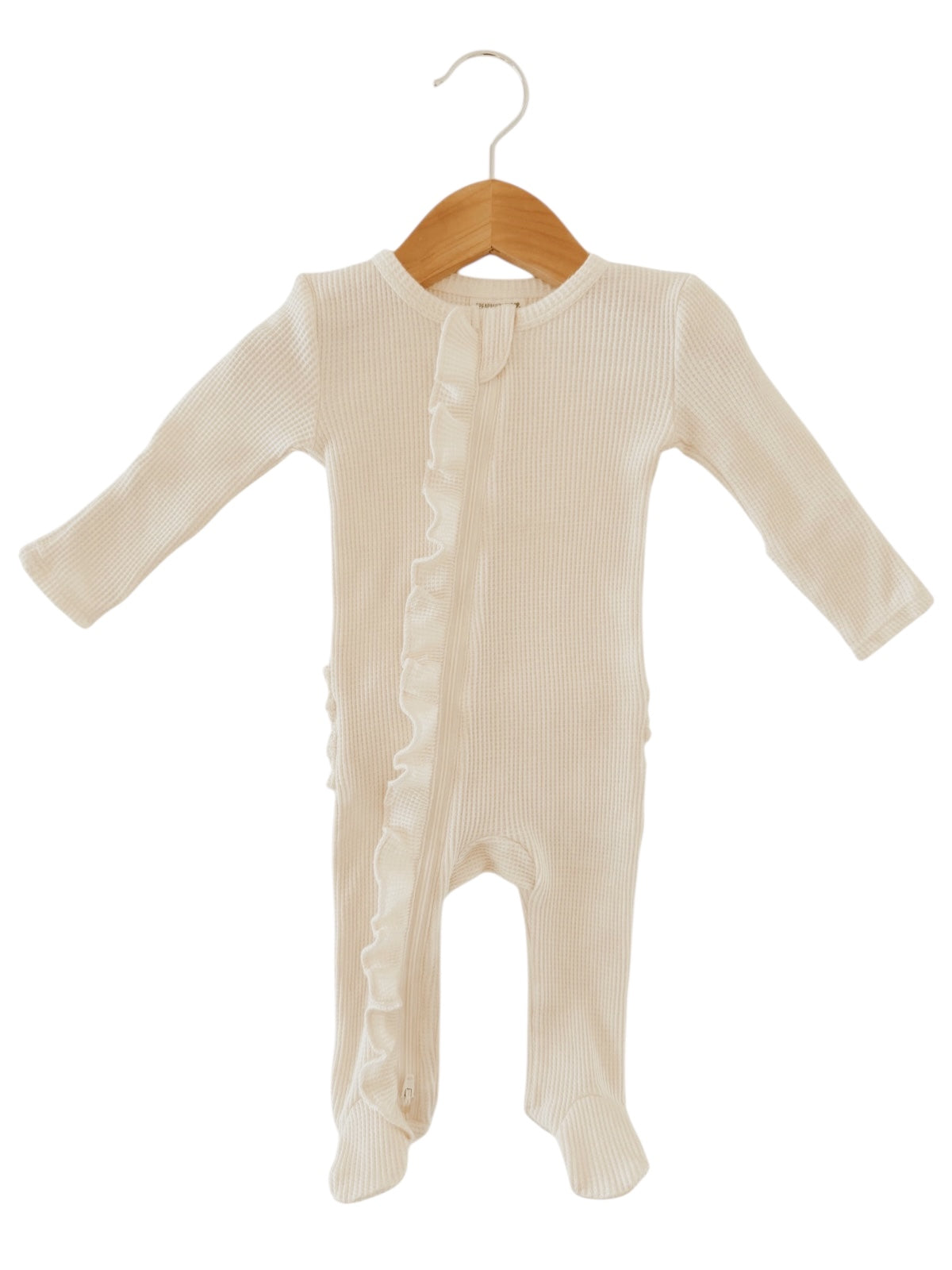 Cream-colored baby onesie with long sleeves and ruffle detail, displayed on a wooden hanger.