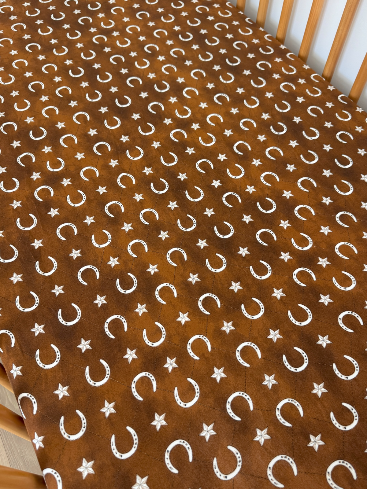 Brown fabric with white crescent moons and stars in a repeating pattern laid on a wooden surface.