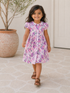 Smiling girl in a floral dress walks on a stone path, with a potted plant in the background.