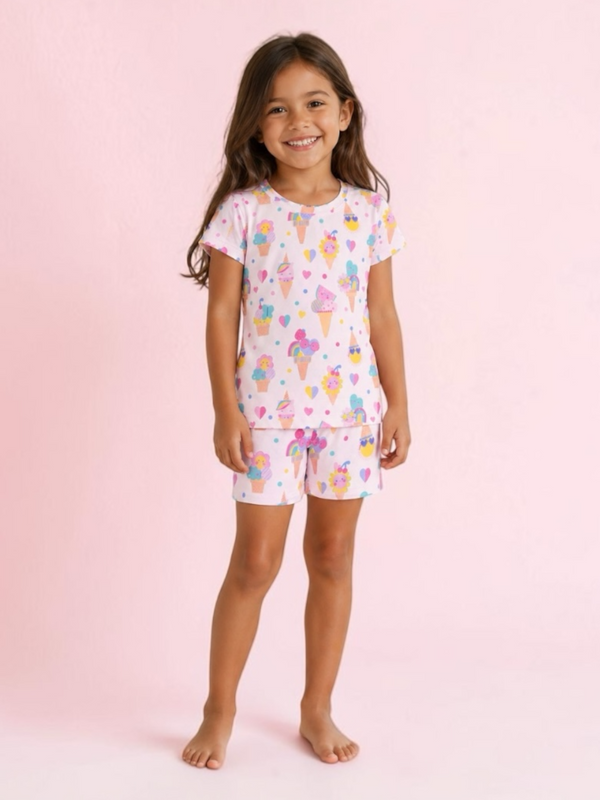 Smiling girl in colorful ice cream-themed pajamas against a pink background.