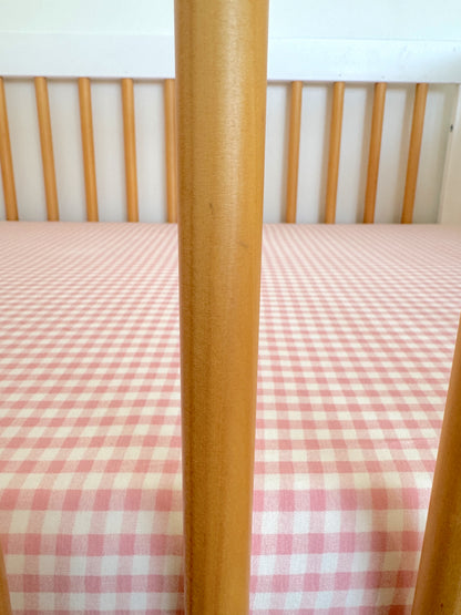 Wooden crib with vertical slats and a pink checkered bedding pattern.