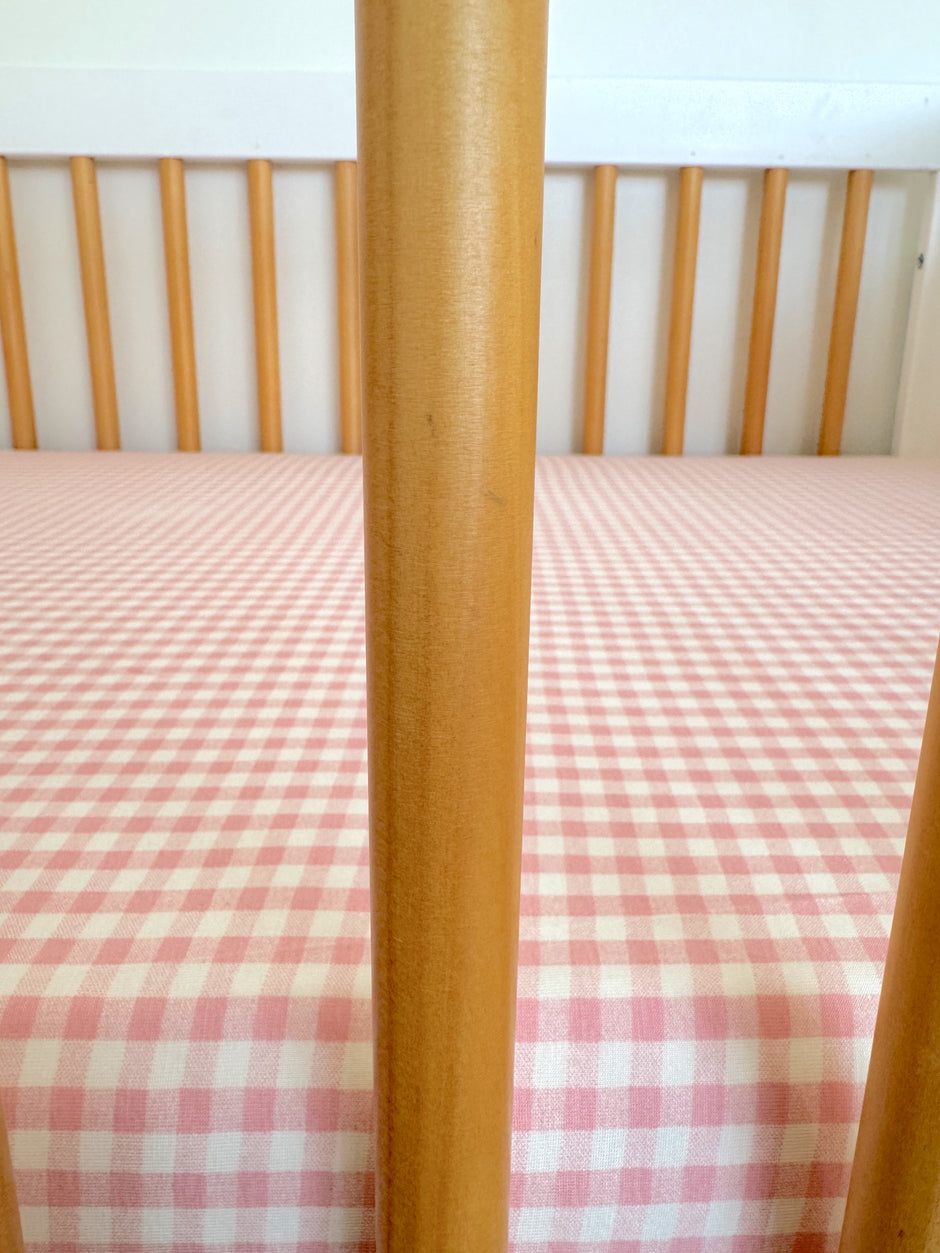Wooden crib with vertical slats and a pink checkered bedding pattern.