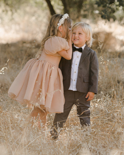 Two young children sharing a moment in a sunlit field, dressed elegantly for a special occasion.