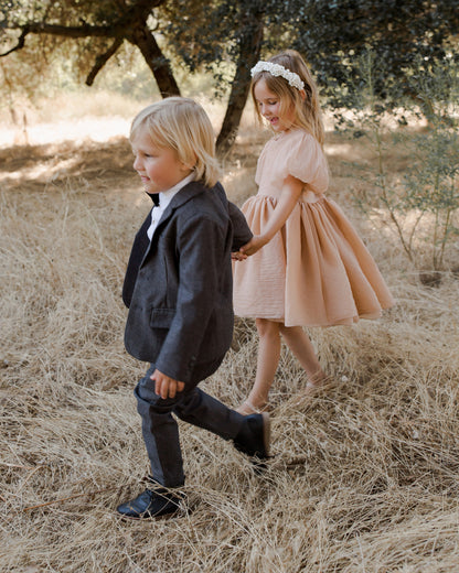 Two children walking hand in hand in a grassy field, dressed in formal attire.