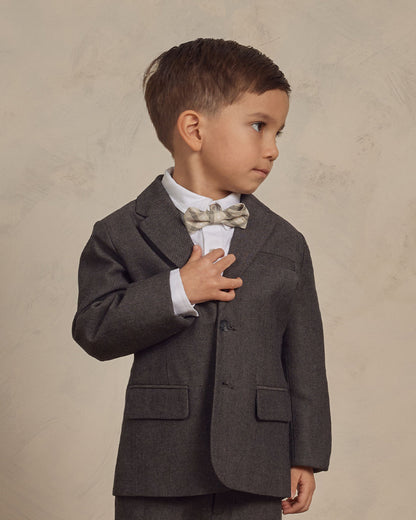 Young boy in a tailored gray suit and bow tie, looking thoughtfully to the side, with a neutral background.