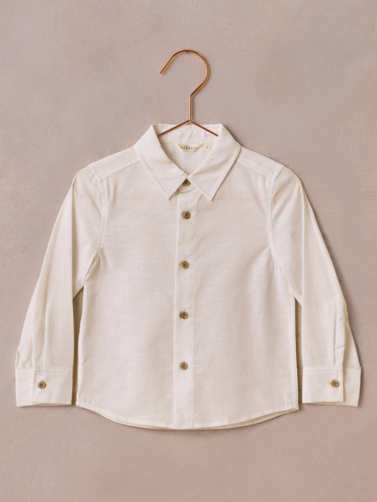 Light-colored long-sleeve button-up shirt hanging against a textured background.