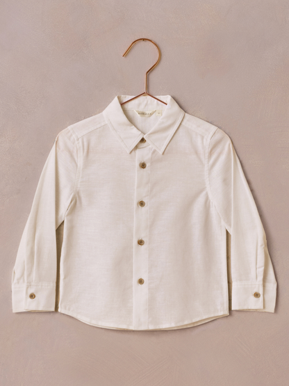 Light-colored long-sleeve button-up shirt hanging against a textured background.