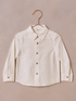 Light-colored long-sleeve button-up shirt hanging against a textured background.