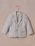 Light gray blazer hanging on a copper hanger against a textured pink background.
