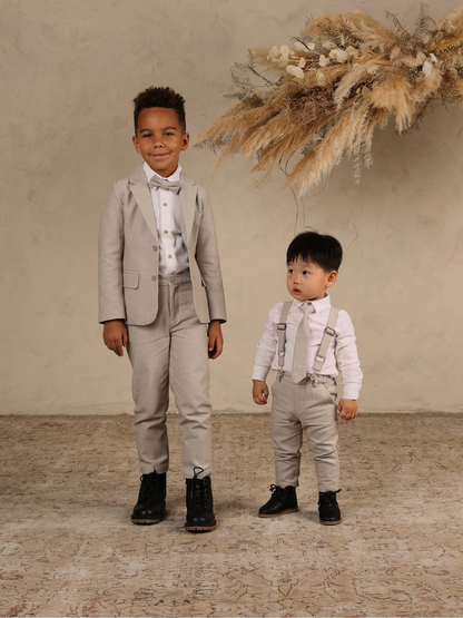 Two young boys in stylish suits pose for a photo, with a decorative backdrop of dried flowers.