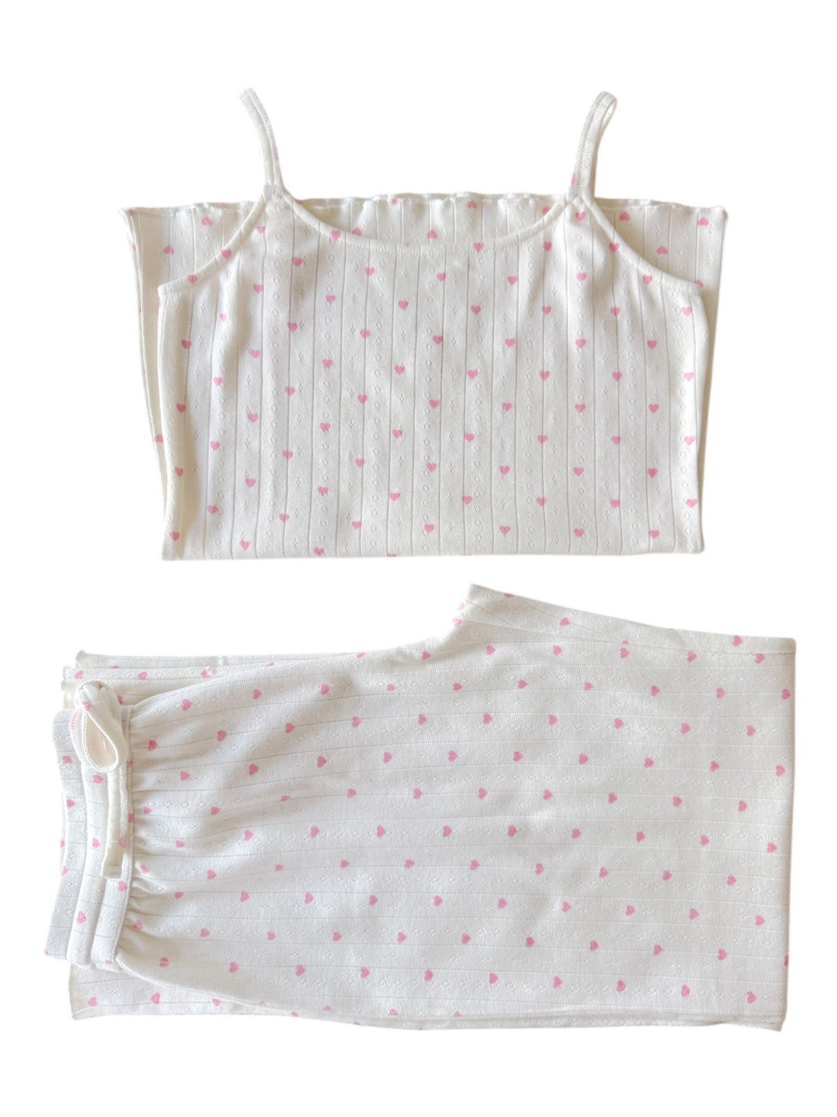 White pajama set featuring a spaghetti strap top and pants with pink heart patterns. Perfect for cozy nights.
