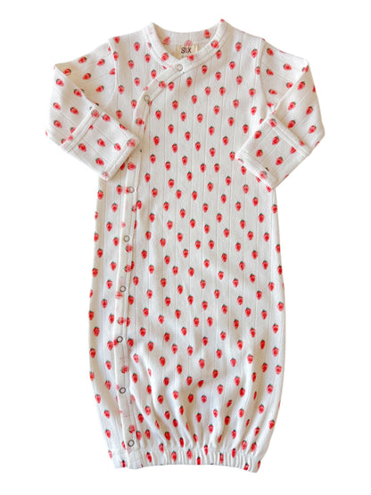 White baby gown with red strawberry pattern, featuring long sleeves and snap buttons along the side.
