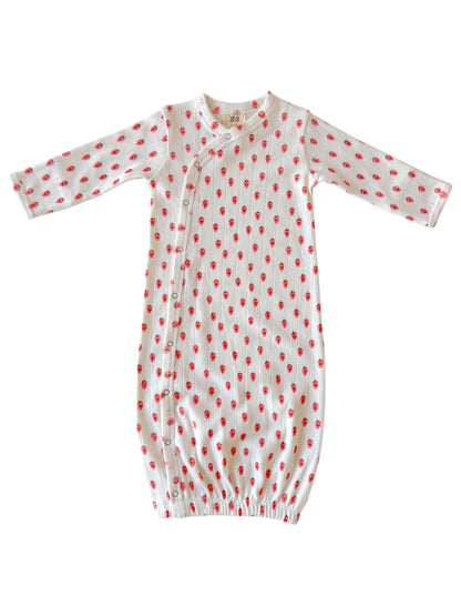 White baby gown with red strawberry patterns and snap buttons, featuring long sleeves and elastic bottom.