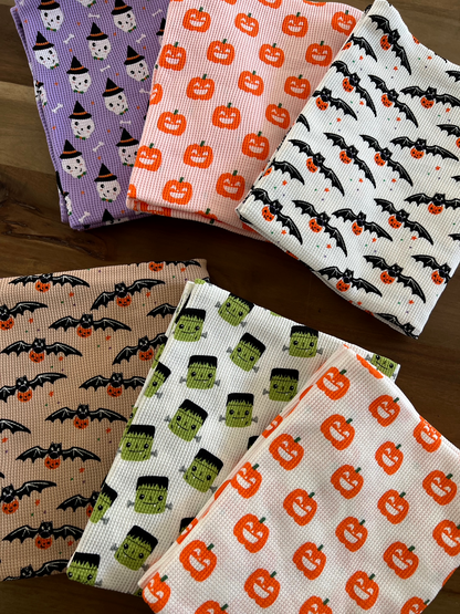 Colorful Halloween-themed fabric pieces featuring pumpkins, bats, and spooky characters arranged on a wooden surface.