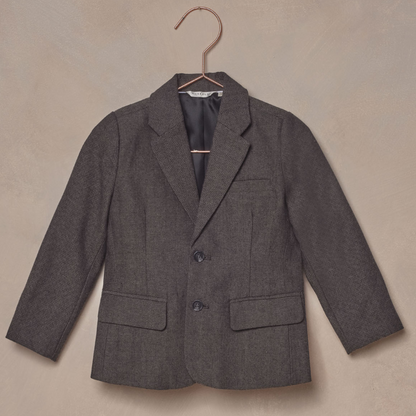 Gray children's blazer hanging on a rose gold hook against a textured background.