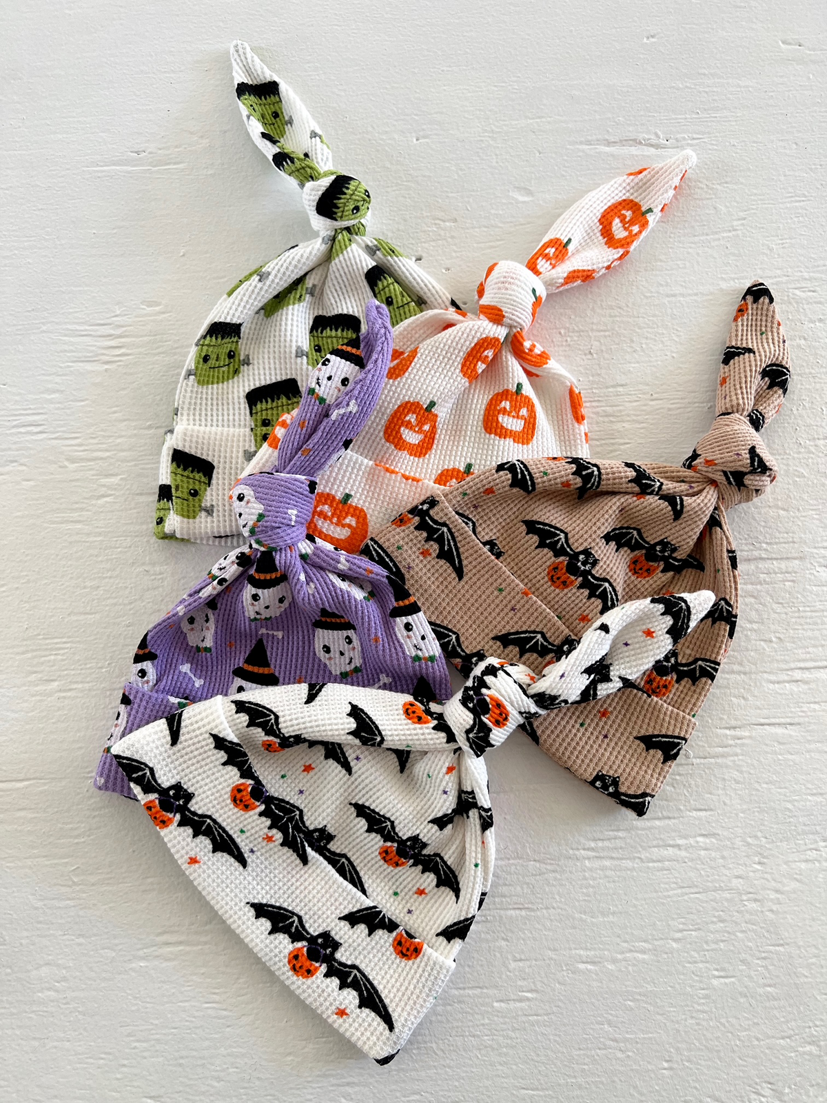 Colorful Halloween-themed baby hats with various patterns, including pumpkins, bats, and monsters, tied at the top.