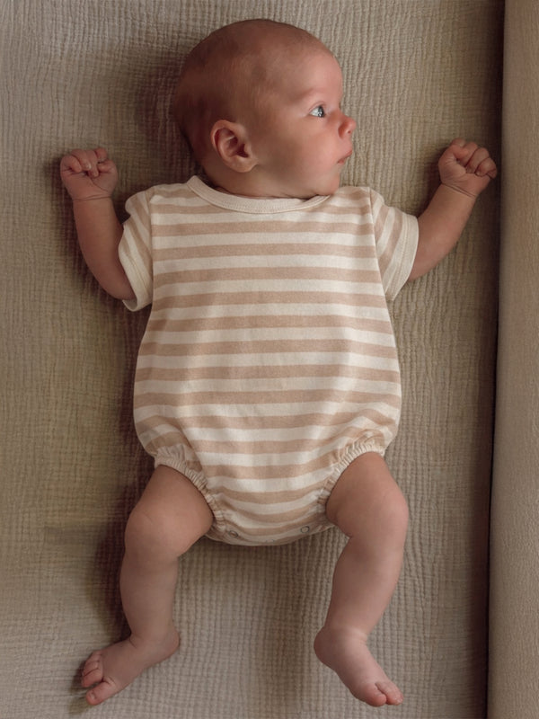 Infant in a striped onesie lying on a textured surface, looking to the side with a curious expression.