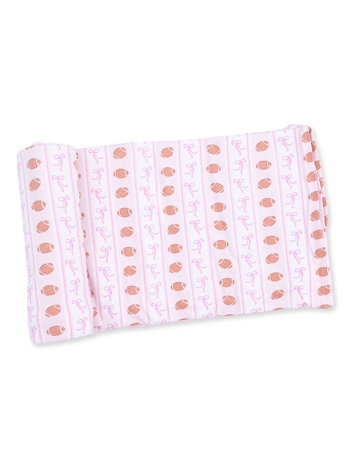 Pink fabric with football and ribbon pattern rolled neatly. Ideal for craft or sewing projects.