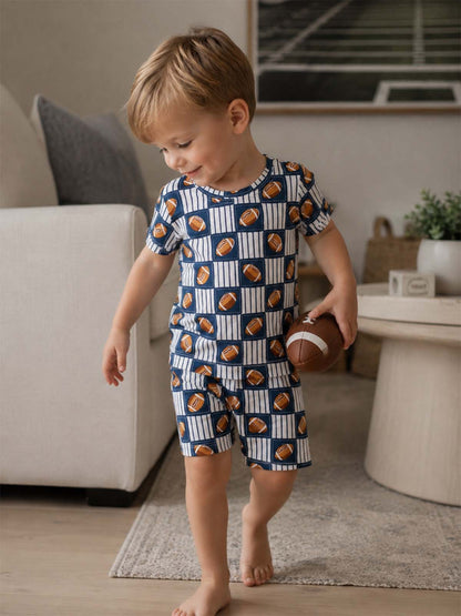 Young boy in pajamas with football print, holding a football in a cozy living room setting.