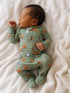 Newborn sleeping on a white blanket, wearing a green onesie with a playful animal print.