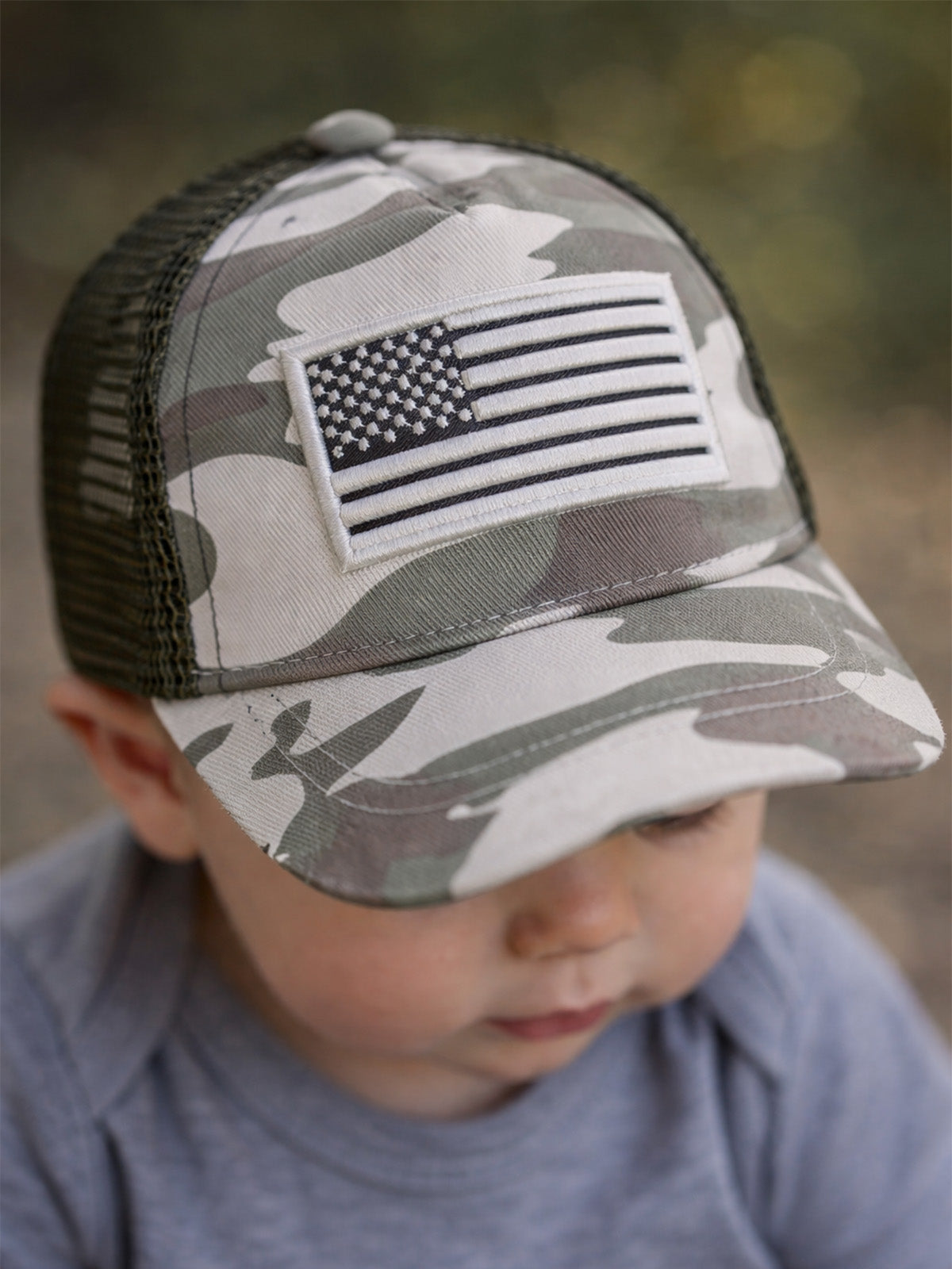 Child wearing a camo cap with an American flag patch, focused on something out of frame.