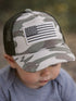 Child wearing a camo cap with an American flag patch, focused on something out of frame.