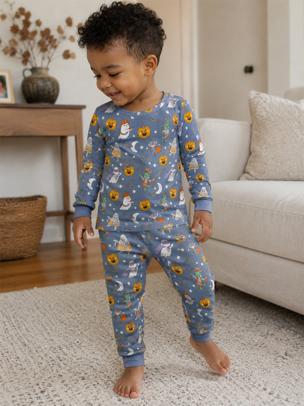 Smiling toddler in playful pajama set with Halloween-themed prints, standing on a rug in a cozy living room.