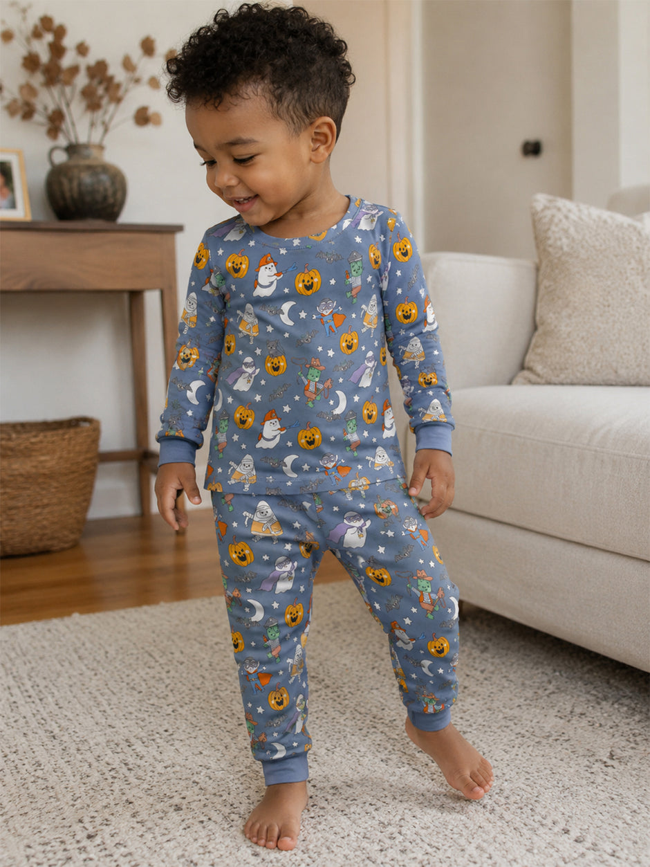 Smiling toddler in playful pajama set with Halloween-themed prints, standing on a rug in a cozy living room.