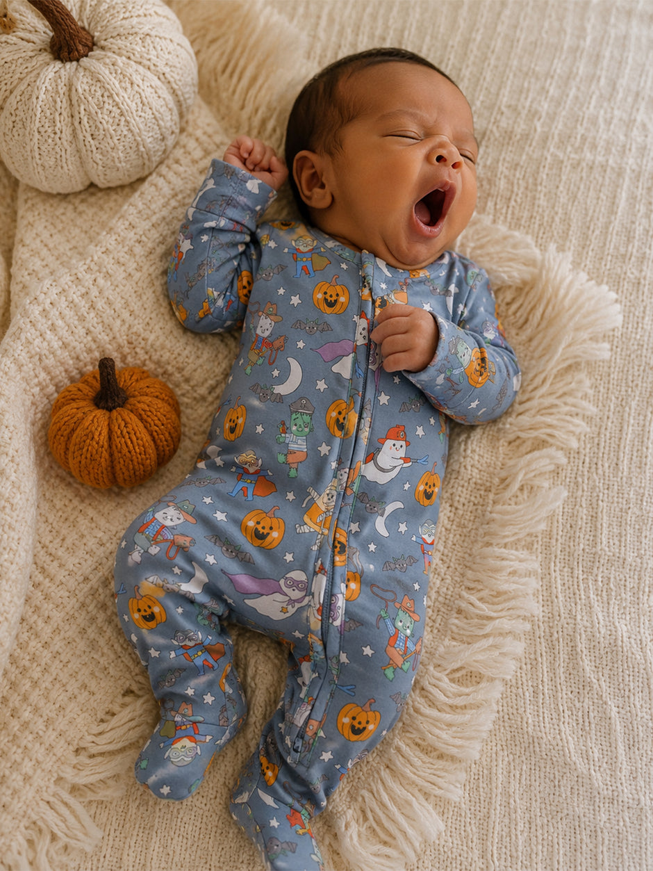 Yawning baby in festive pajamas on a textured blanket with pumpkins and autumn decor.