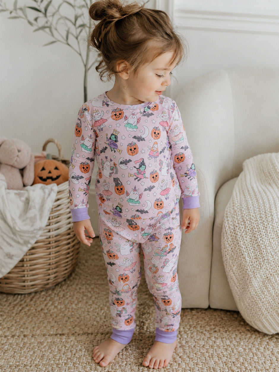 Toddler in Halloween-themed pajamas with pumpkins and ghosts, standing beside a cozy basket and plush toys.