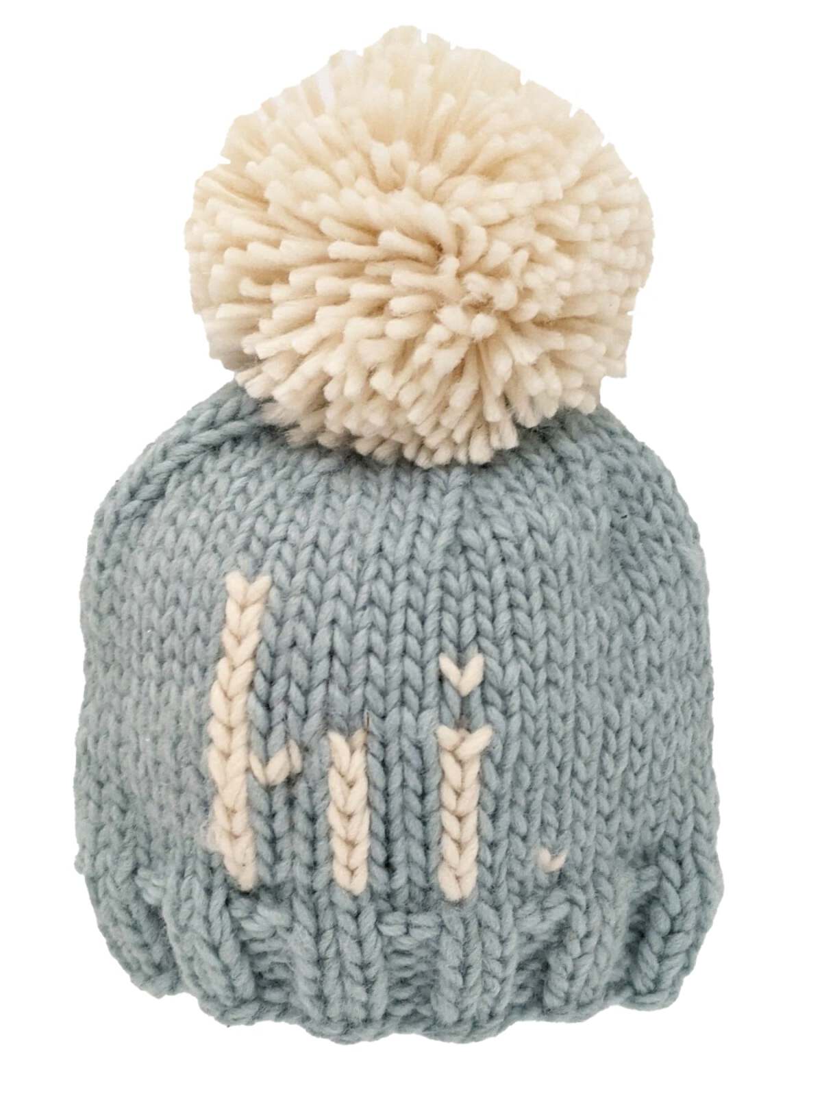 Light blue knitted beanie with a large cream pom-pom and the word "Hi" embroidered on the front.