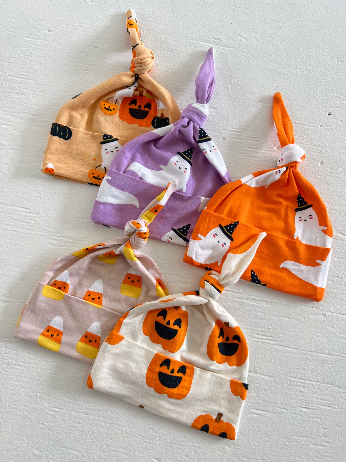 Five colorful baby hats featuring Halloween designs like pumpkins and ghosts, neatly arranged on a white background.