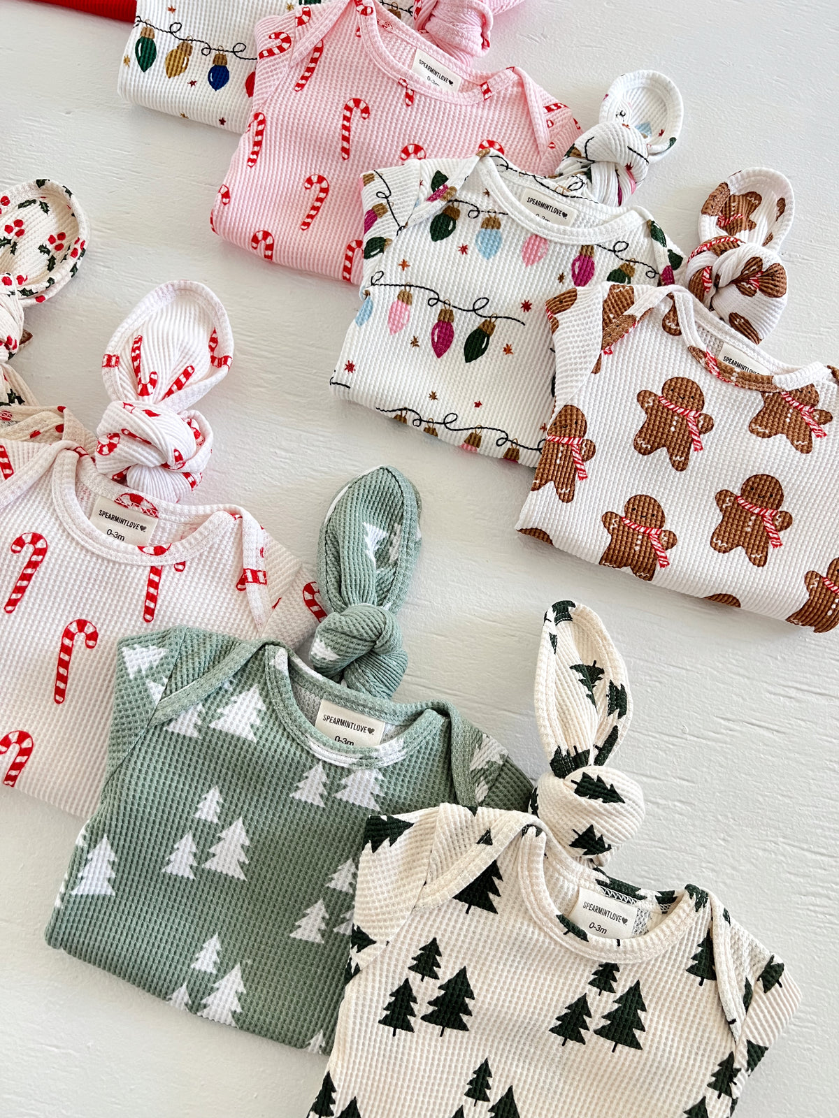 Colorful baby outfits with festive patterns including candy canes, Christmas lights, gingerbread, and trees.